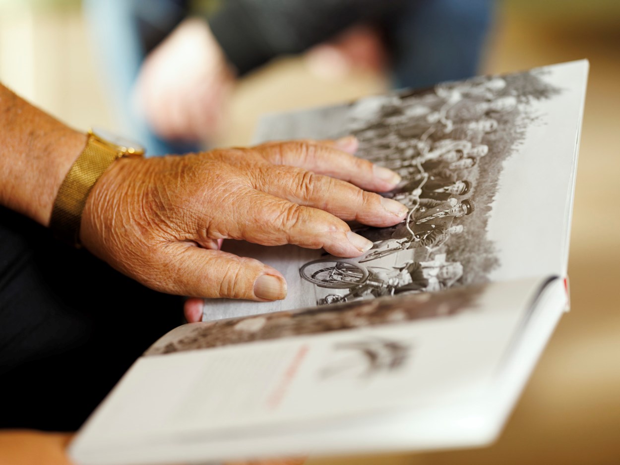 En äldre persons hand som ligger på en bok med svartvitt foto..