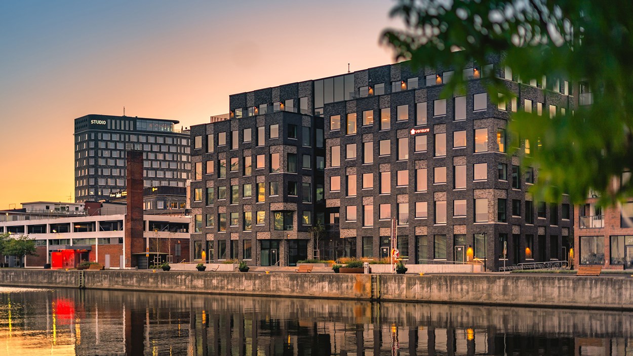 Kontorshus på en kaj med vatten framför. Bakom syns en högre byggnad avteckna sig not en rosa-gul himmel. get på Universitetsholmen i Malmö och är konstruerat med människans välmående i fokus.
