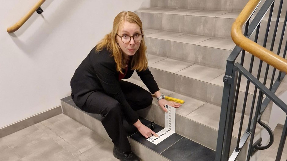 Kvinnlig arkitekt kontrollerar handledare och kontrastmarkeringar i en trappuppgång.