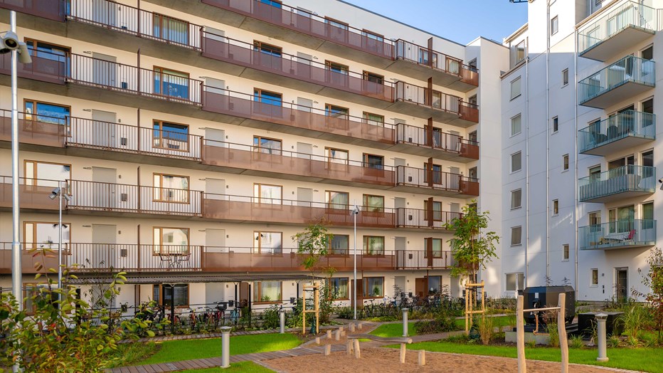 Grön innergård med plats för avkoppling, gemenskap och aktiviteter. Innergård med lekpark, gräsmatta och träd omringad av bostadshusens fasader
