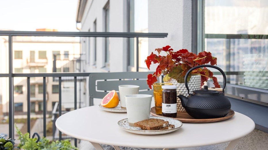 Här byggs stora sociala lägenheter som bjuder in till att leva hållbart. Kvarteret har till exempel både bil och cykelpool. Balkong med dukat runt bord och utsikt över innergård samt grannhus.