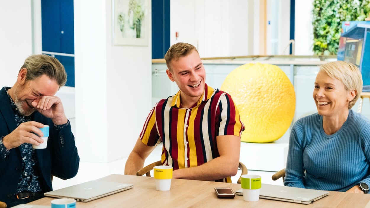 Tre glada medarbetare som sitter vid ett bord och skrattar tillsammans.