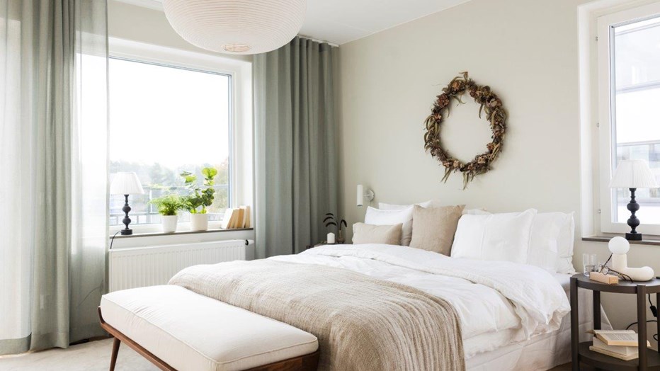 Att bo i Scilla innebär ett behagligt, smart och grönt sätt att leva.  Sovrum med säng i ljusa färger på sängkläderna. Två fönster åt olika väderstreck.