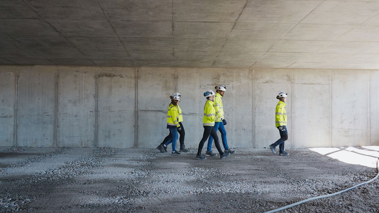 Betongvägg med fyra varselklädda personer som går tillsammans.