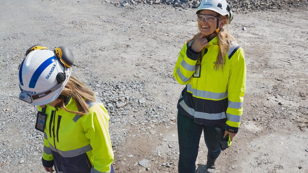 Två studenter i vita hjälmar och varselkläder som ler.