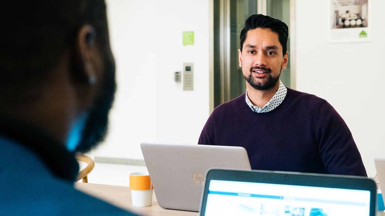 Två personer som sitter vid laptops och pratar med varandra.