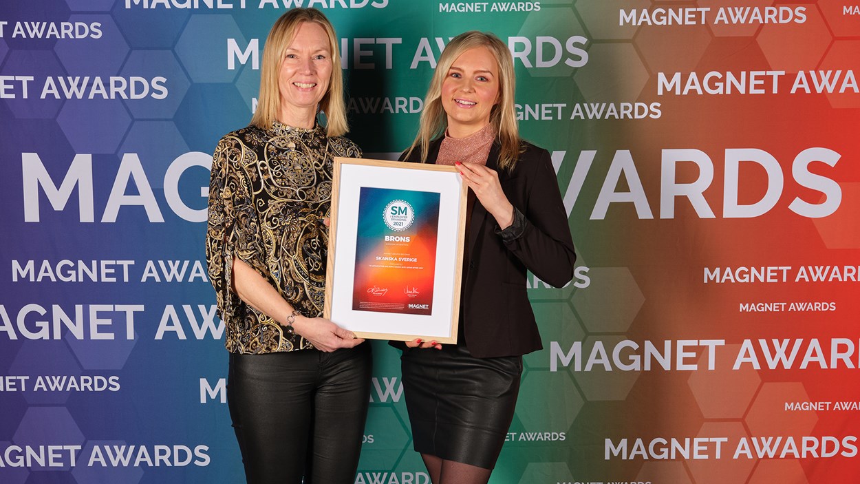 Två glada kvinnor som håller i ett diplom mot bakgrund där det står Magnet Awards