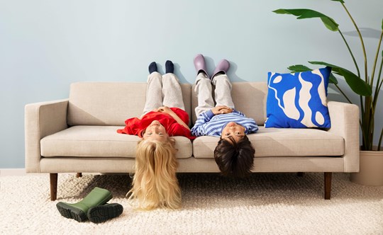 Två barn ligger upp och ner i en soffa och tittar in i kameran. 