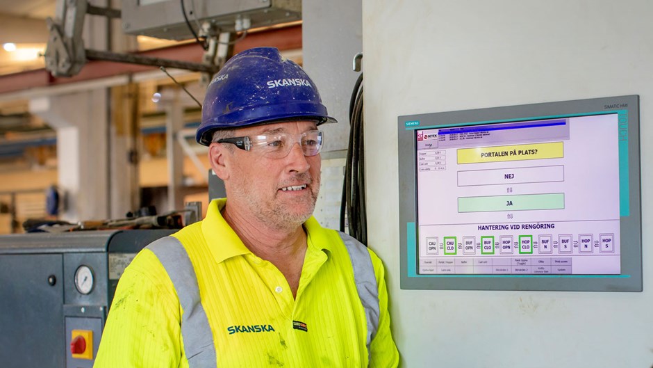 Simon Mahoney är en av pålfabrikens operatörer. Via kontrollpanelen sköter han maskinen som häller rätt mängd betongmassa i gjutformarna med exakt precision. Via sin mobiltelefon sköter han också det dagliga underhållet av maskinen. Foto: Emelie Asplund