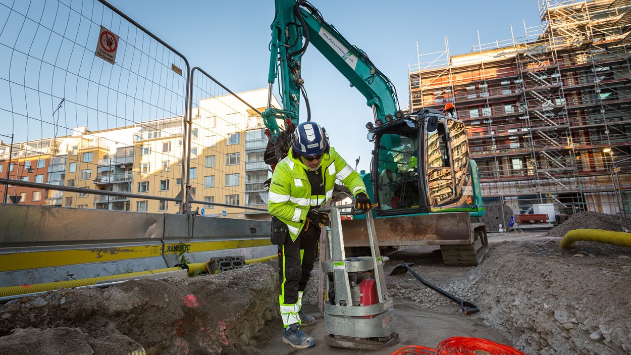 Man i gula varselkläder jämnar till en betonggjutning på marken med en vibratorplatta.