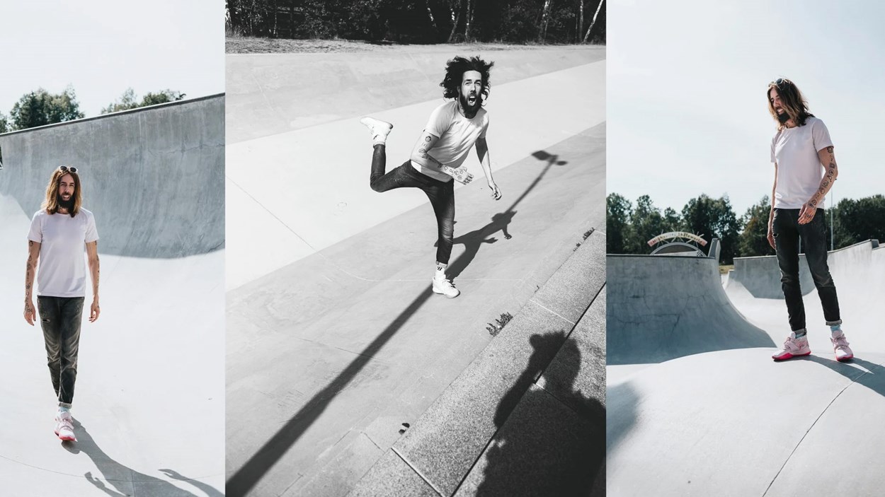 Man i jeans, vit t-shirt och gympaskor som går, står och hoppar i en skateborardramp i betong.