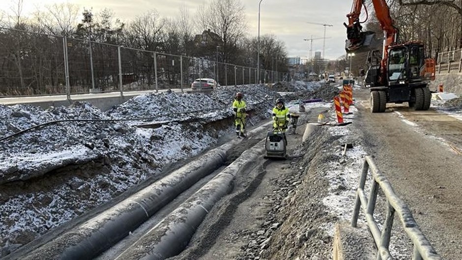 Skanskas yrkesmedarbetare jobbar med att platta till och göra fyllnadsmaterialet kompakt runt en fjärrvärmeledning.