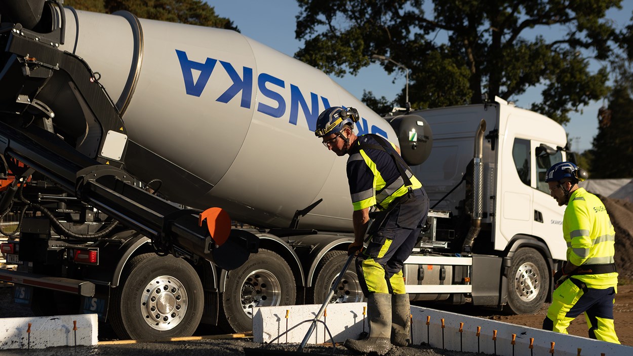 Person i varselkläder som jämnar till betong under gjutning. I bakgrunden syns en betongbil.