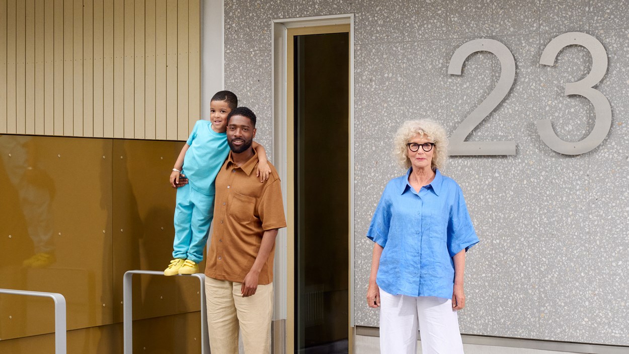 Tre generationer med äldre kvinna, medelålders man med barn framför en husfasad.