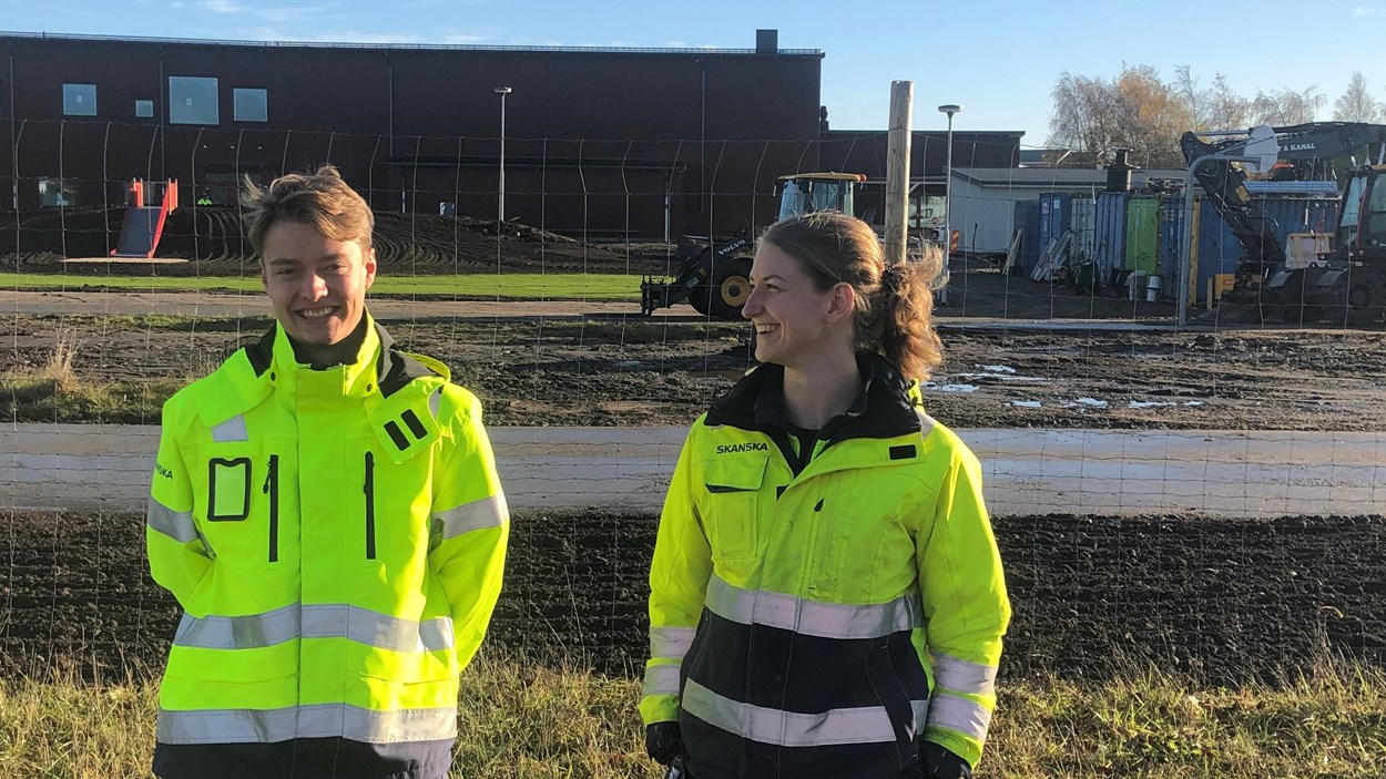 En kille och tjej i varselkläder, i bakgrunden syns en skolbyggnad.