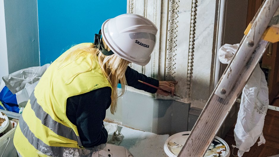 Kvinnlig byggarbetare målar en list vid renoveringen av Nationalmuseum.