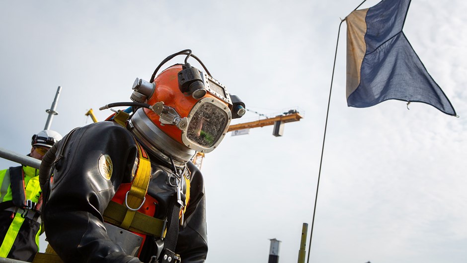 Dykare Mark Buinkhunst står med full tungdykarutrustning som väger närmare 40 kilo. I bakgrunden syns den hissade dykarflaggan.
