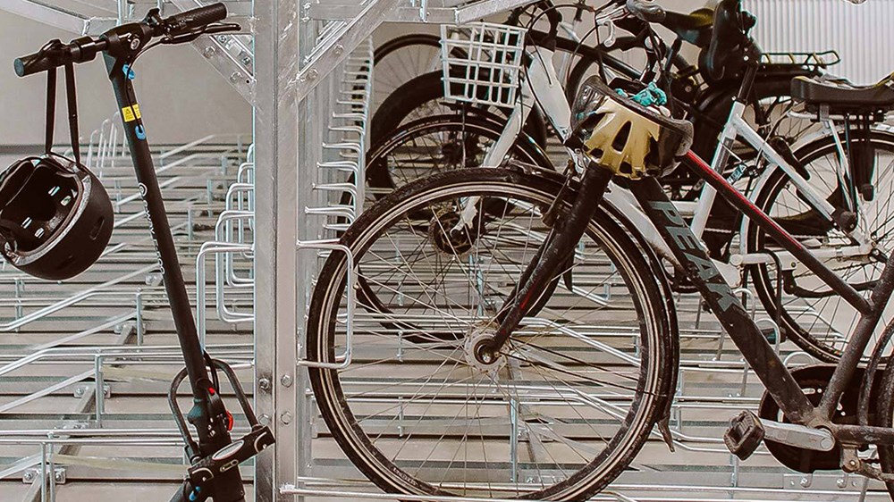 En sparkcykel med hjälm på styret och flera cyklar uppställda i ett cykelgarage.
