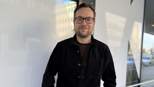 Porträtt på Skanskas kalkylingenjör Mattias Persson framför ett blänkande fönster.