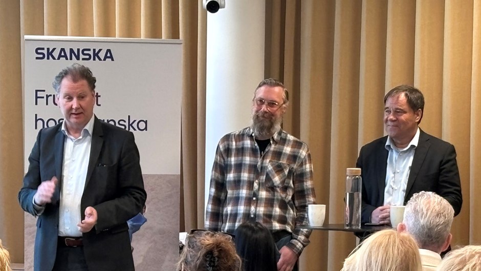 Tre män står framför publik och talar.