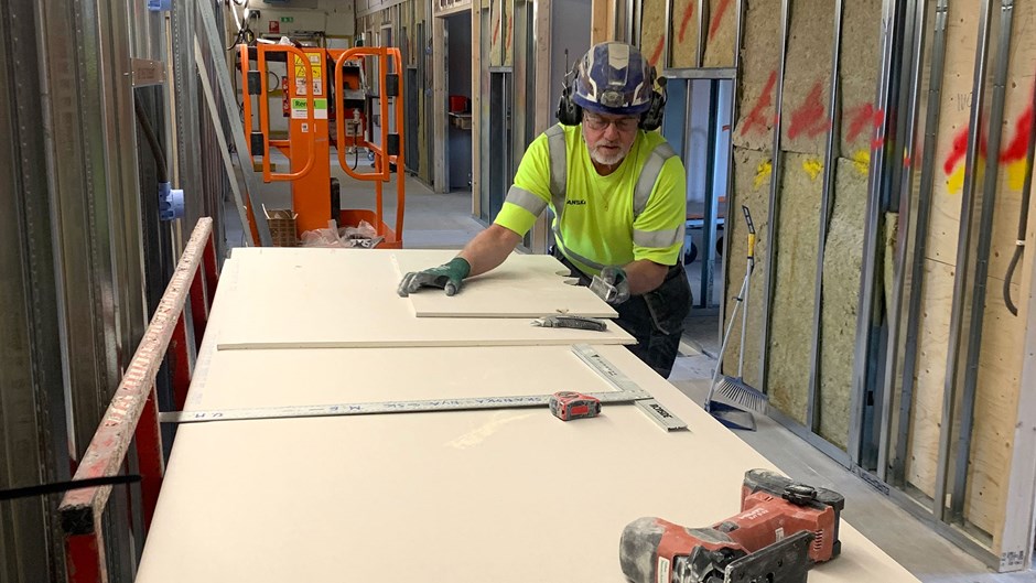 Byggarbetare sågar plywoodskivor i en korridor.