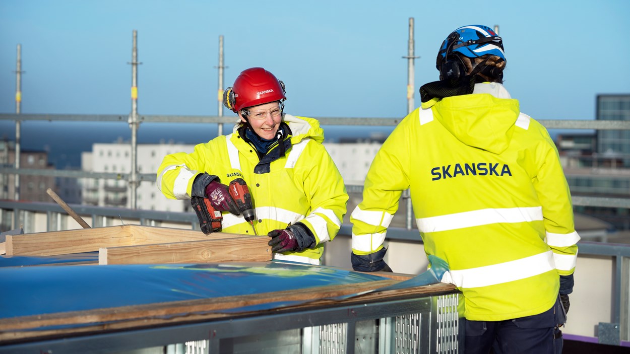 Två personer gula skydskläder och hjälmpar som är vända mot varandra i samtal.