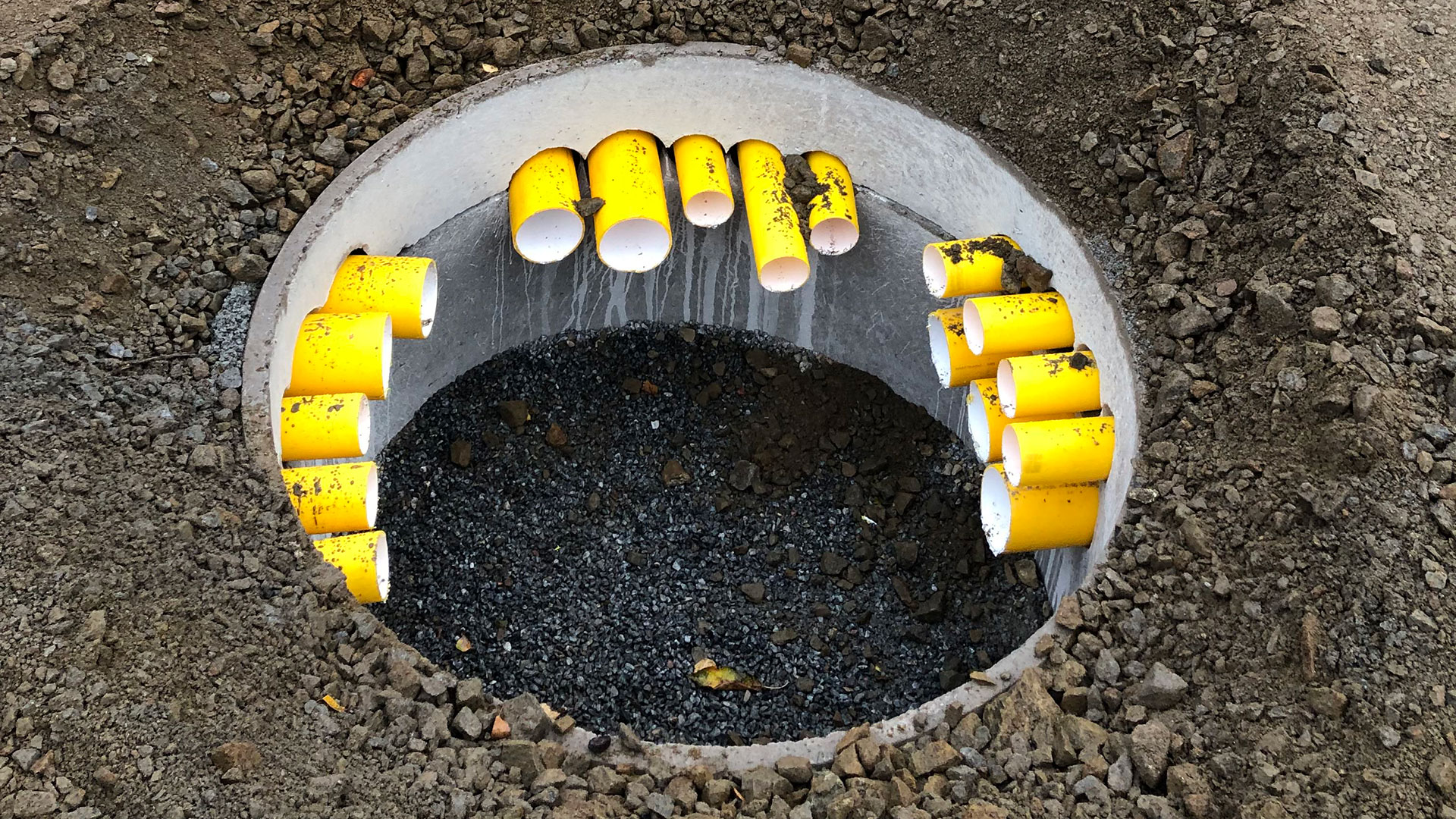 Nedgrävd kabelbrunn med gula kabelrör som en del av Skanskas elektrifieringsprojekt för elbussar vid Gubbängens och Nybodas bussdepåer.