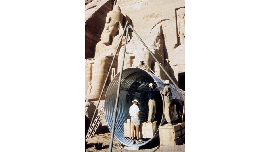 Man i shorts och tropikhjälm står i ingången till ett egyptiskt tempel.