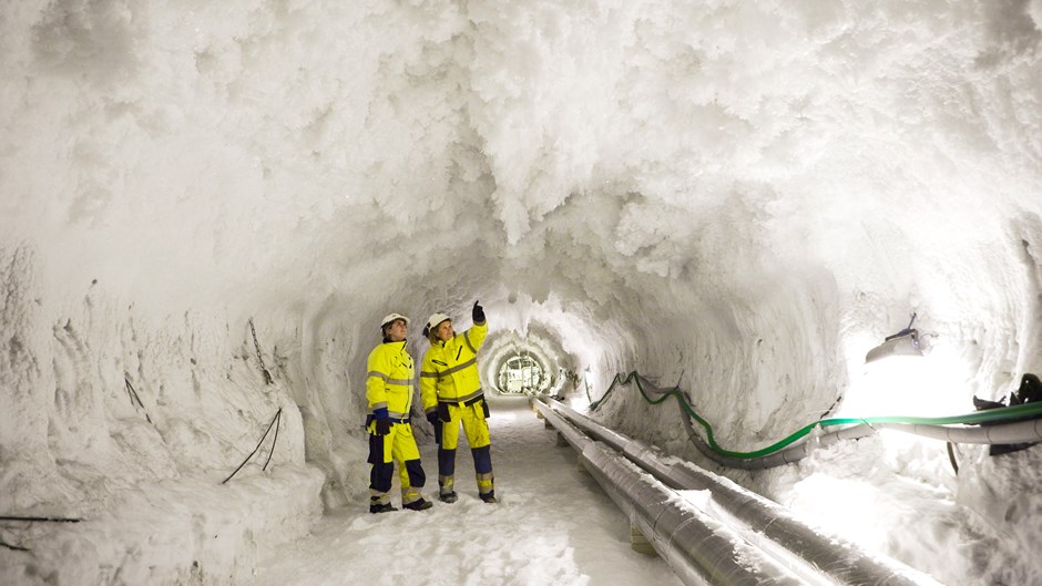 Två byggarbetare står i en tunnel täckt av is.