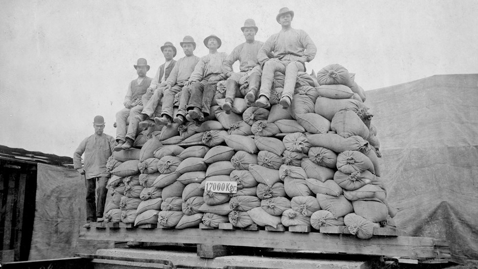 Sju arbetare sitter på en hög med betongsäckar på en bild från 1800-talet.