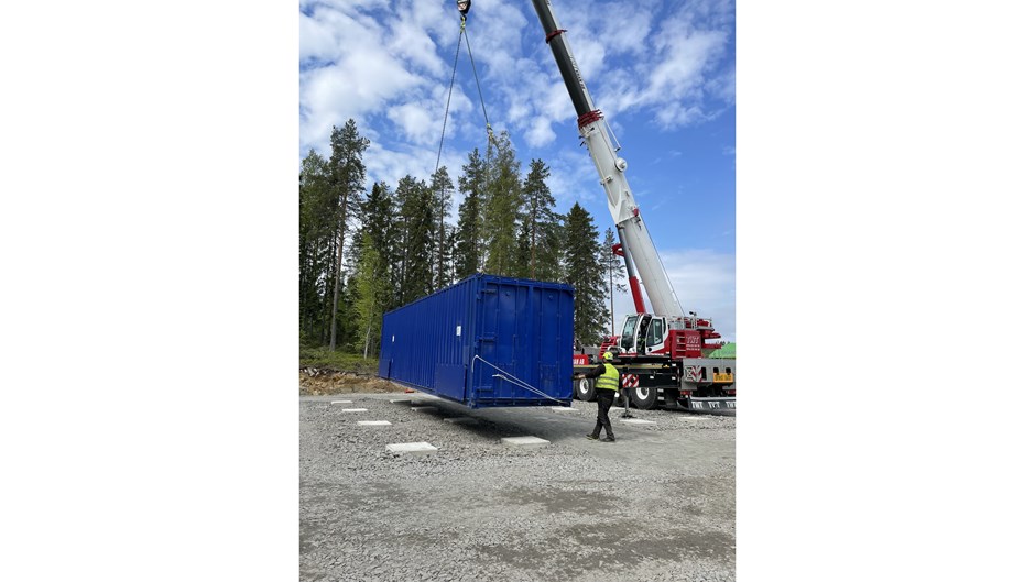 En lyftkran lyfter en blå container.  