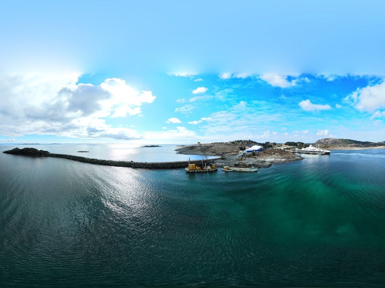 Klippöar under en blå himmel på ett grönt hav. Flytbrygga med kran framör öarna.