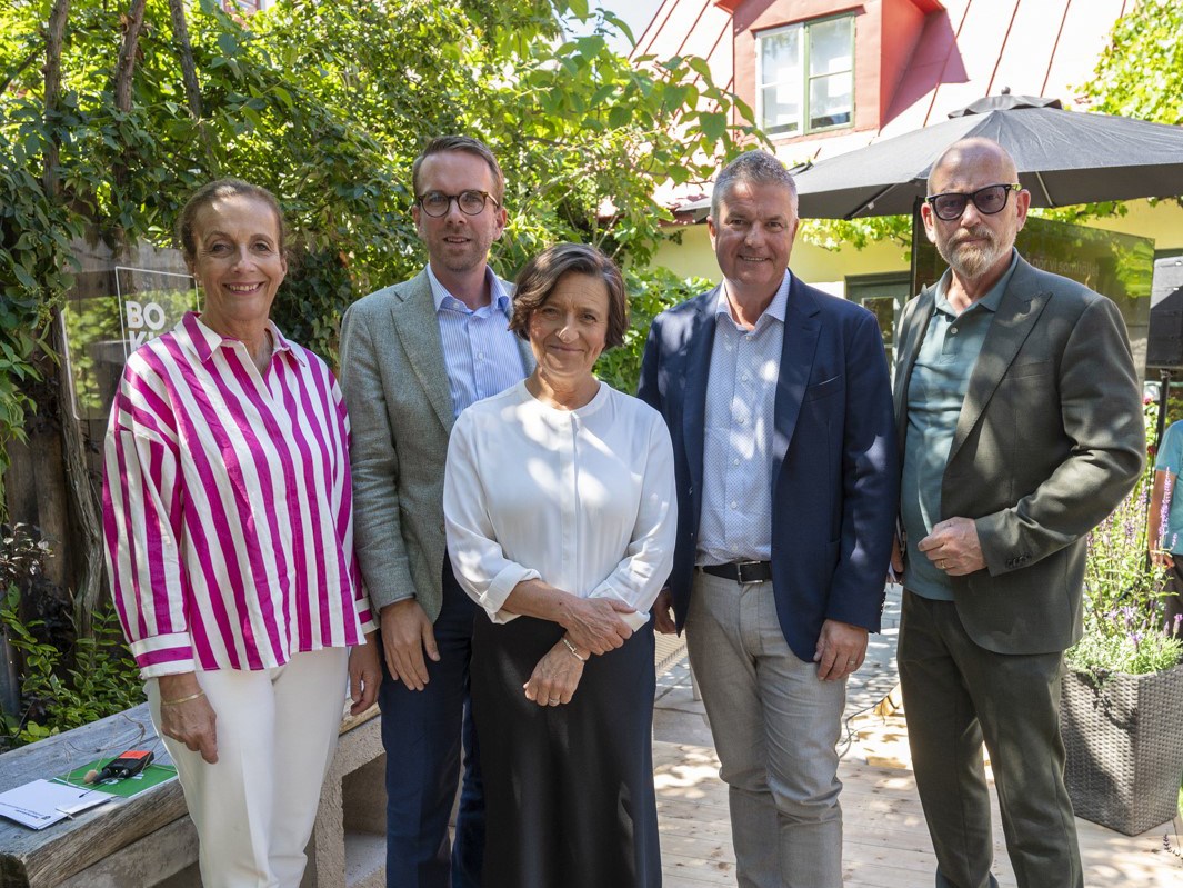 En kvinna och fyra män som ler på en scen mot en bakgrund av grönska.