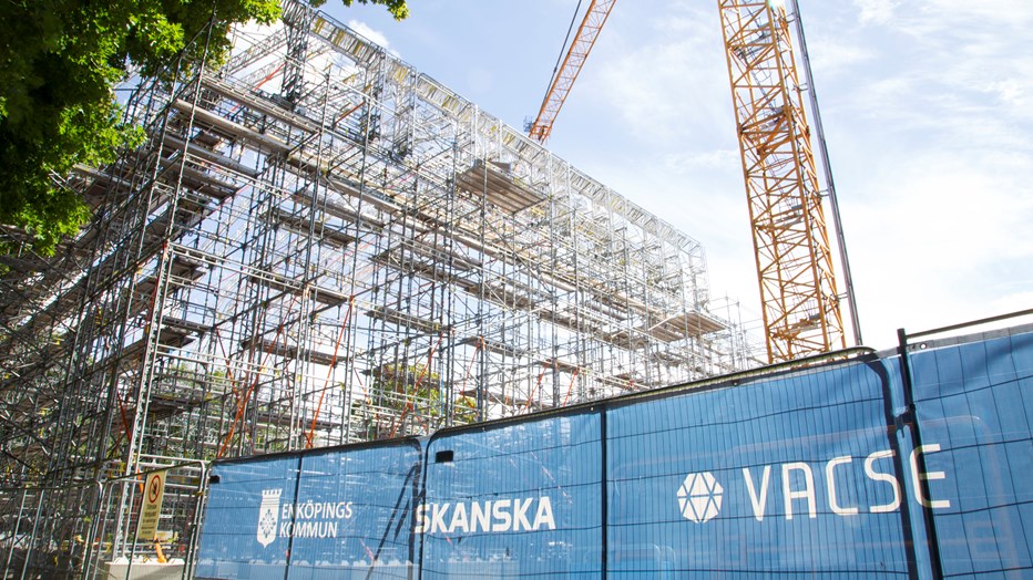 Väderskyddet hjälper till att skydda konstruktioner från regn och fukt samt förbättrar arbetsmiljön för byggarbetarna. Foto Jessica Lindegren, Enköpings kommun Ställning som bildar väggar och tak monteras med hjälp av em byggkran. I förgrunden syns stängsel med skyltning och loggorna Skanska och Vacse.