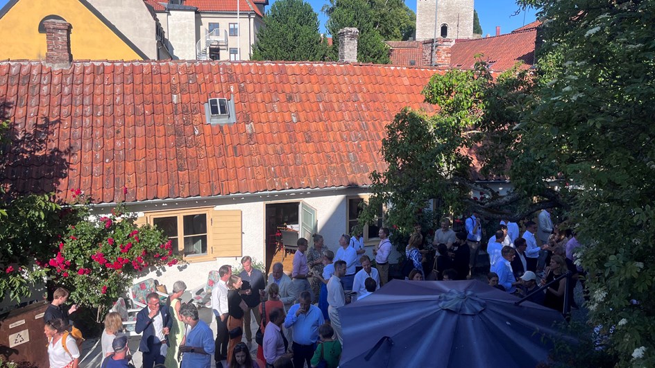 Många pesoner som minlgar i trädgården med mat och dryck i trädgården sett ovanifrån. I bakgrunden syns Visbys hustak.