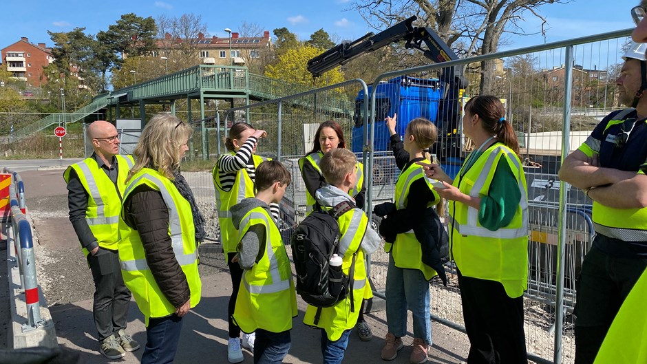 Skolelever och lärare i gula varselvästal lyssnar till personal från Skanska som pratar.