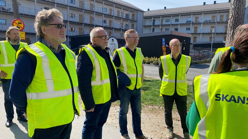 Män i gula varselvästal står och lyssnar till personal från Skanska.