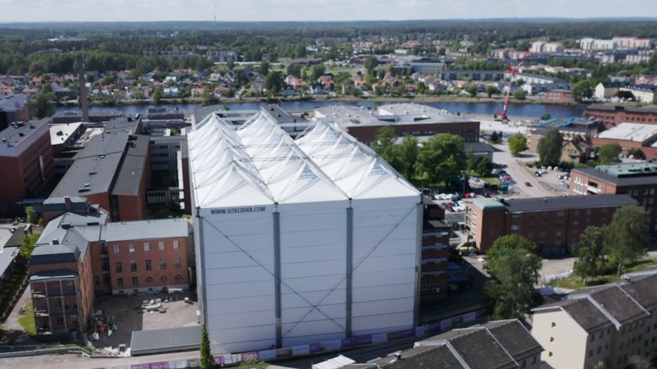 Under väderskyddet fortsätter arbetet med nya mottagningshuset för Karlstad centralsjukhus precis som vanligt, oavsett väder. En typ av stort vitt tält uppsatt över bygget.