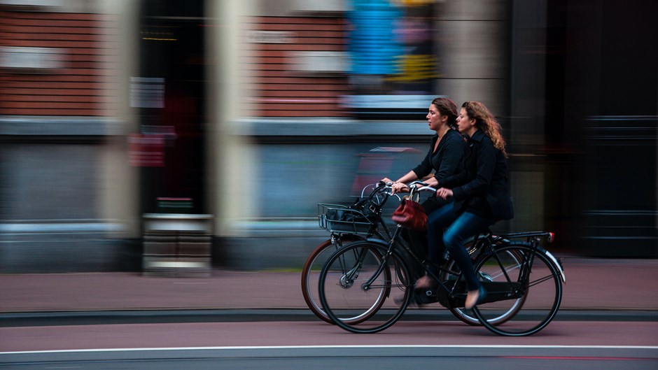 Två kvinnor cyklar i stadsmiljö.