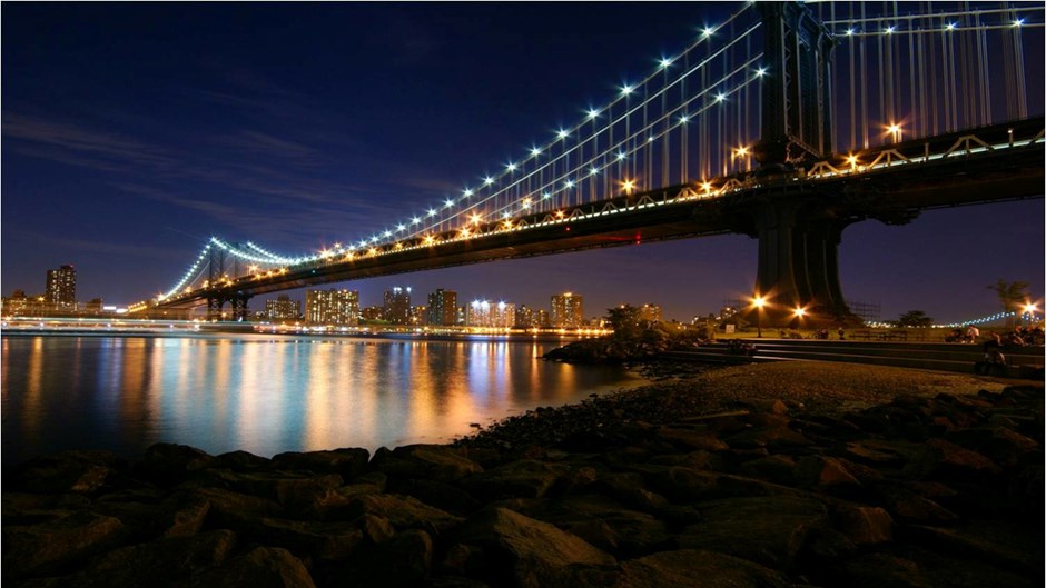 Nattlig vy över Manhattanbron i New York som är upplyst av lyktor efter hela brospannet.