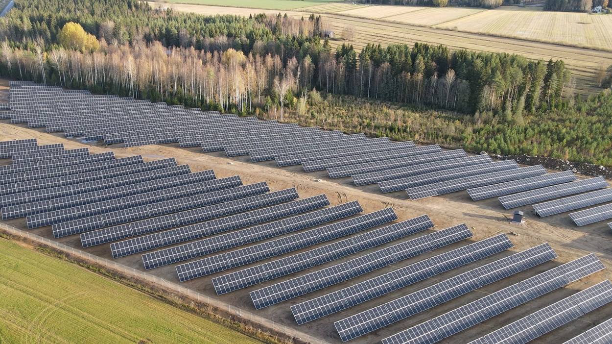 Solcellsanläggning där svarta solpaneler står på rad ute på en stor gräsyta.