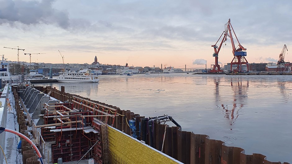 Schakt för kajen med pålar i stål intill vattnet. I bakgrunden syns Göteborgs stad och bebyggelse, bro och hamnkranar.