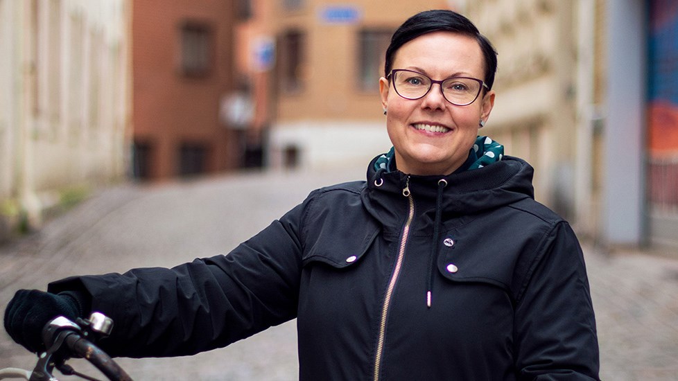 Leende kvinna med mörk jacka står bredvid en cykel.