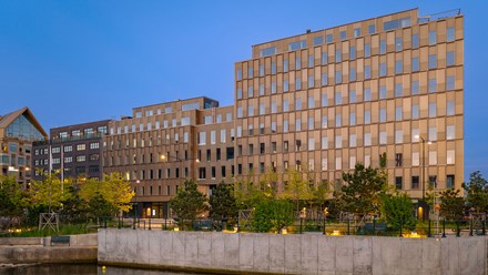 Aqua kontorsfastighet i Malmö Kontorsfasad i brunt mot blå himmel. Framför går en gata som delvis skyms av träd en kaj med vatten i förgrunden.