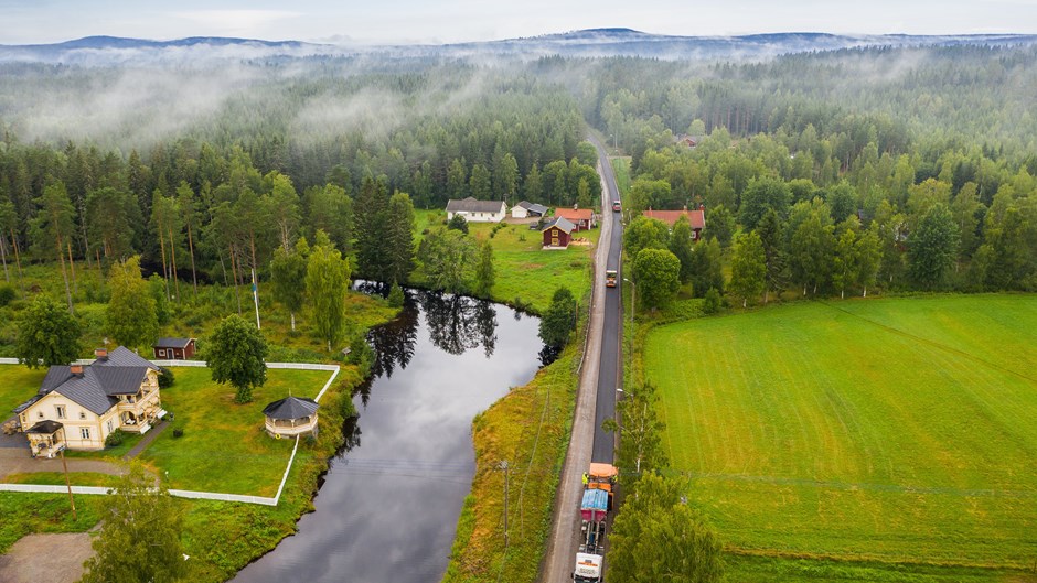 Asfalt rullas ut och på vägen står en lastbil. Runt omkring vägen är det skog och öppna landskap.