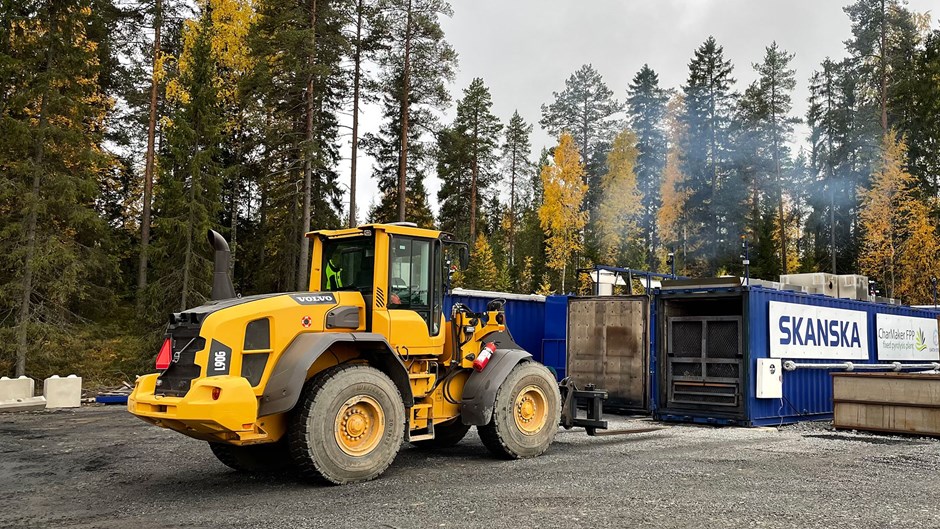 En gul grävmaskin kör in mot biokolpannan.