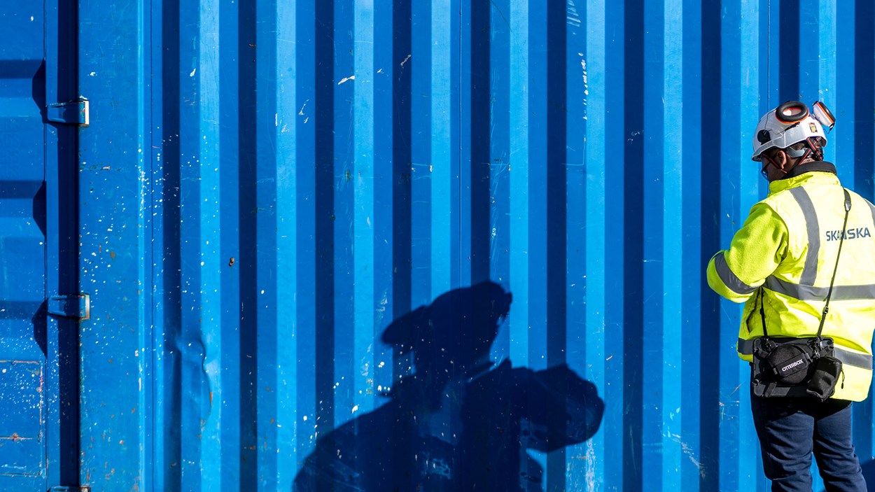 Byggnadsarbetare som speglas i en blå container.