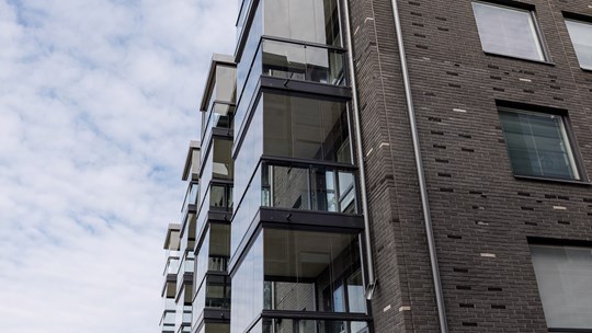 Fasaden på ett nybyggt bostadshus med fönster och balkonger sett nerifrån.