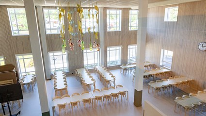 Matsalen har högt i tak, stora fönster och träinredning som skapar en varm atmosfär.