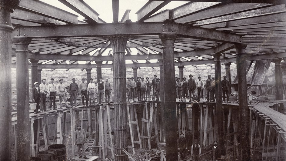 Svartvitt foto av arbetare som står inuti en rund byggnadsställning i trä .